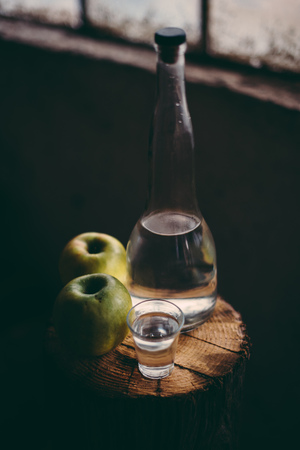 Apple brandy, rustic retro atmosphere. Bottle and single shot glass with alcohol drink and two green apple fruit.の写真素材