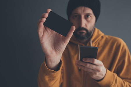 Casual man showing blank mock up credit card as copy space, holding mobile phone in other hand for...