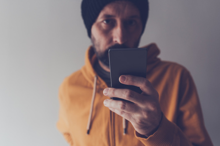 Casual adult male with cap and yellow hooded shirt looking at mobile phone, low key communication...