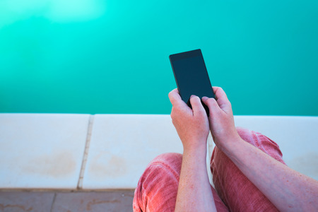Using mobile phone by the swimming pool, female hands holding smartphoneの写真素材