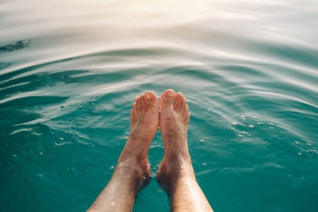 Male feet in outdoor swimming pool. Man enjoying refreshing poolside water in summer sunset. Holidays vacations and weekend activities.の写真素材