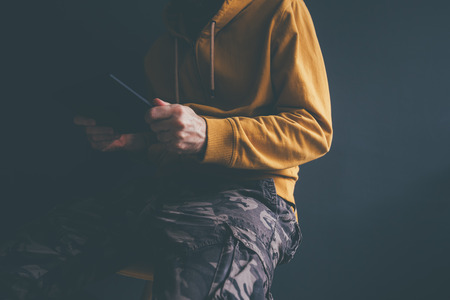 Casual man using digital tablet laid back in office chair. Male person wearing yellow hoodie and military trousers is using modern computer device.の写真素材