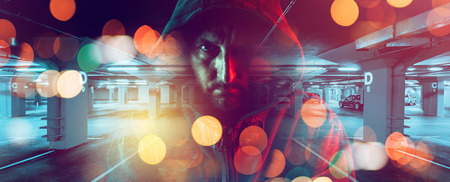 Car thief conceptual image with hooded criminal man overlaying image of underground parking garage