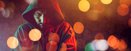 Hooligan with hoodie in urban surrounding, low key portrait of hooded male person at city streets at nightの写真素材