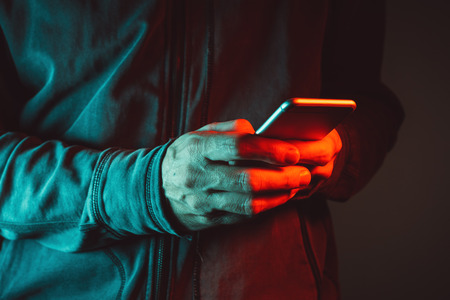 Modern communication concept, close up of male hands typing text message on smartphone, red and blue lit imageの写真素材