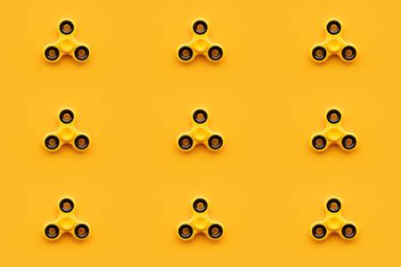 Seamless pattern background of yellow fidget spinner toy on same color backdrop, minimalistic retro style compositionの写真素材