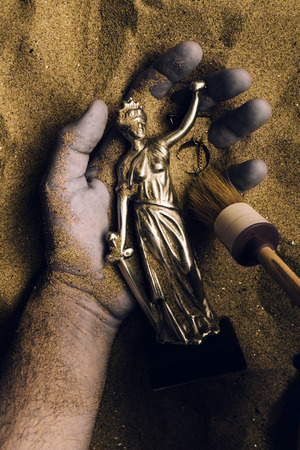 Forensic expert discovering dead body buried in desert sand with Justice statue in hand. Conceptual image for police investigation of an cold case murder crime scene.の写真素材