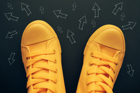 Making decisions and right choices conceptual image with yellow sneakers on the road with small arrow imprints pointing to various directionsの写真素材