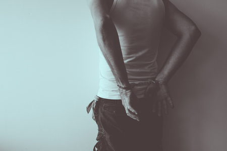 Duotone image of gang member under arrest with handcuffs put against the wall, conceptual image
