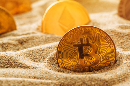 Golden bitcoin in sand, conceptual image for lost and found valuable cryptocurrency coins that are standing the test of time.の写真素材