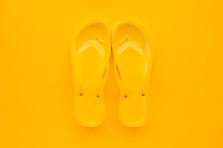Top view of yellow flip flops pair on same color background with copy space. Beach sandals or slippers in minimalistic warm summer toned composition.の写真素材