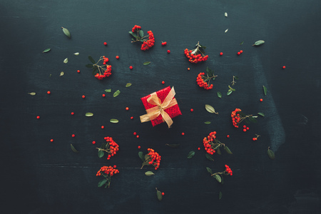Flat lay anniversary present gift box with red wrapping and golden ribbon on dark background with floral arrangement, top viewの写真素材
