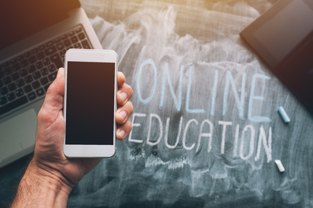 Online education concept with hand holding smartphone over laptop and tablet computer