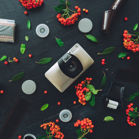 Vintage retro camera flat lay on dark background decorated with negative film rolls and wild berry...