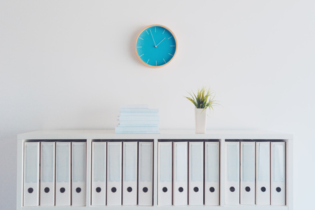 Modern bright business office interior detail depicting wall clock and shelf with books, plant and...