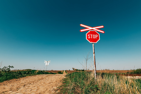 Crossbuck and stop sign on countryside road and railway intersection against blue sky