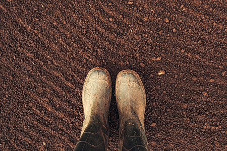 Top view of farmer rubber boots standing on ploughed arable land with copy space