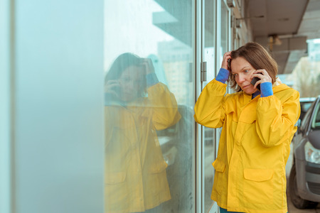 Sad woman in yellow raincoat talking on mobile phone out on the street while it's rainingの写真素材