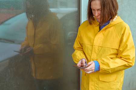 Woman in yellow raincoat texting on mobile phone outdoors on rainy day