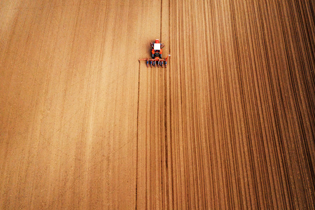 Drone photography of tractor with seeder working in field, agricultural machinery is planting seed into freshly plowed landの写真素材