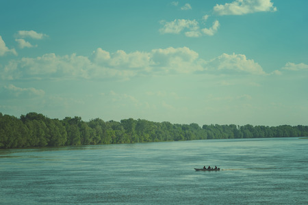 Small fishing boat on Danube river with three unrecognizable peopleの写真素材