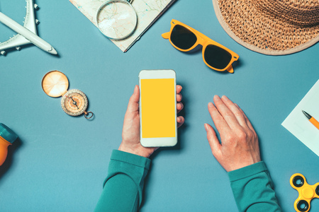 Smartphone mock up in summertime holiday vacation concept, woman holding mobile phone with blank screen as copy space, top view overhead shot with flat lay arranged summer accessories