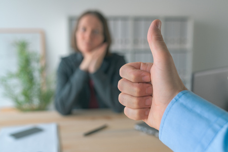 Satisfied boss gesturing thumbs up to female employee in business office, selective focus on hand endorsing workerの写真素材