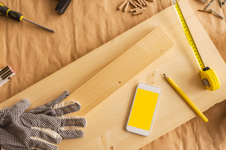 Modern white smartphone with blank screen mock up in small business woodwork carpentry workshop, top viewの写真素材