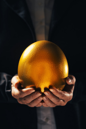 Successful businesswoman holding golden egg as symbol of business opportunity and successの写真素材