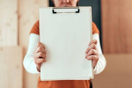 Female carpenter holding clipboard note pad paper mock up copy space in small business woodwork workshopの写真素材