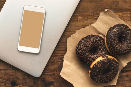 Smart phone mock up and chocolate doughnuts on table, top view of sweet sugary snack next to modern...