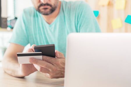 Online shopping with credit card and smart phone, casual man is using smartphone app in home office...