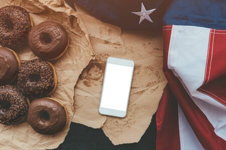 Smart phone mock up with chocolate donuts and USA flag on table in morning, top viewの写真素材