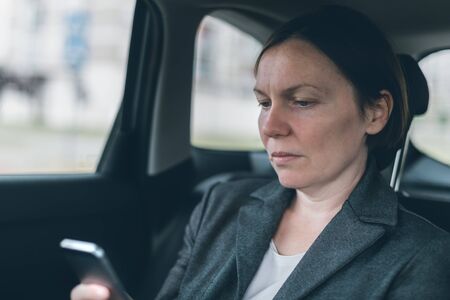 Businesswoman text messaging on mobile phone in car while sitting at the back seat, selective focus