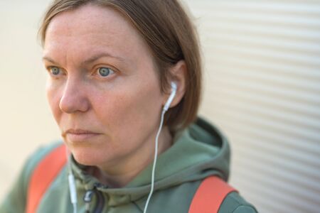 Urban female person listening to music on earphones on street, portrait of casual adult woman...