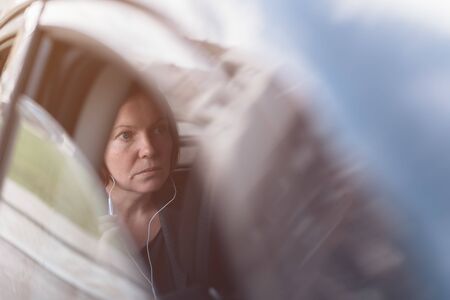 Businesswoman dictating into smartphone earphones microphone while sitting at the back seat of...