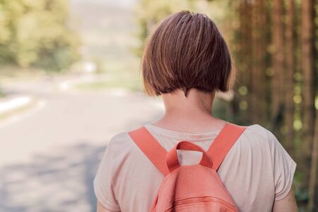 Female hiker walking by the road through countryside, rear view of woman hiking down the roadway on...
