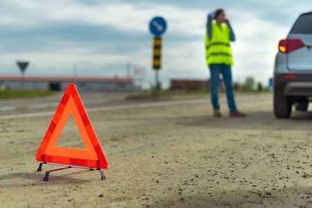 Vehicle breakdown and warning triangle on the road, woman using phone to ask for help and roadside...