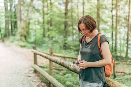 Female hiker text messaging on mobile phone somewhere in forest on trekking pathの写真素材