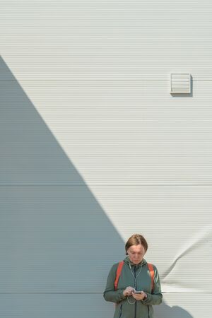 Female jogger using smartphone for text messaging on street while standing next to the wall in urban surroundingの写真素材