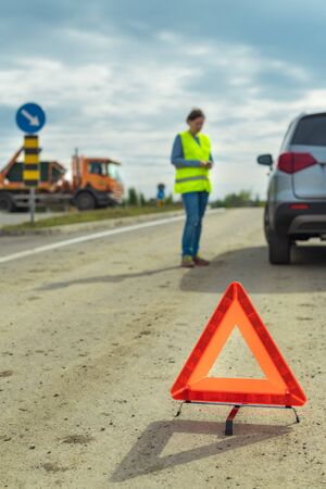 Vehicle breakdown and warning triangle on the road, woman using phone to ask for help and roadside...
