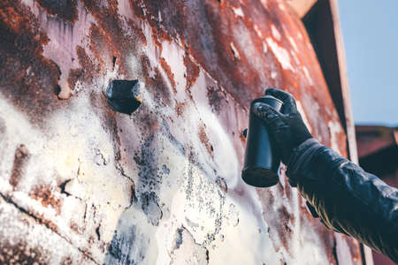 Homeless man spray painting old train wagon with aerosol can. Unrecognizable male person hand close up in conceptual image with selective focus.の写真素材