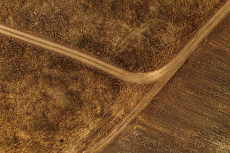 Aerial view of dusty dirt road through grassy plain landscape, top view from drone pov