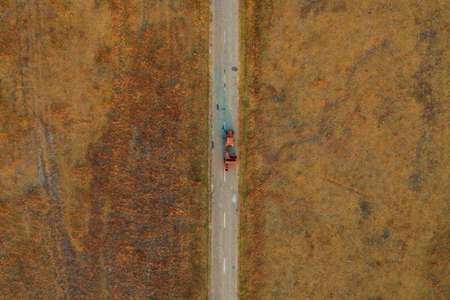 Old tractor on worn asphalt road through grassy countryside meadow, directly above from drone povの写真素材