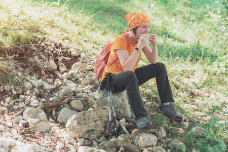 Female hiker eating sandwich in nature, taking a break from trekking outdoor activity and enjoying...