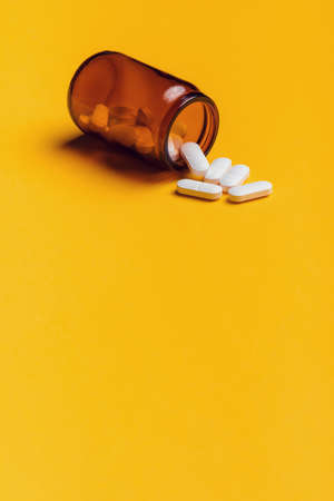 Film coated white oval pills spilled from bottle on yellow background with copy spaceの写真素材