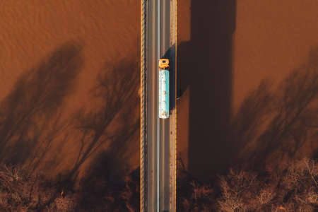 Aerial view of tank truck on bridge crossing the river, directly above drone povの写真素材