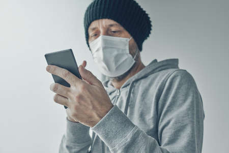 patient using mobile phone for communication while being self-isolated in quarantine. Adult male standing by the window and typing text message.の写真素材
