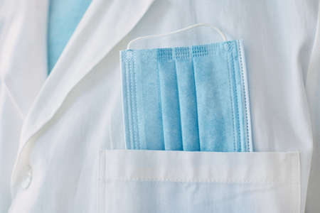 Medical professional with protective face mask in white coat pocket, closeup with selective focusの写真素材
