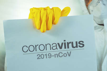 Coronavirus warning paper banner held by male epidemiologist in protective clothingの写真素材